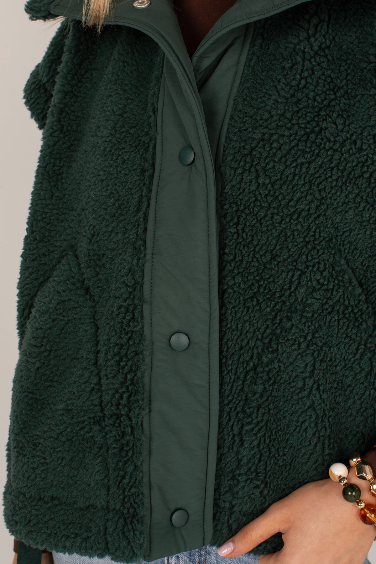 Close-up of a dark forest green fleece jacket with a snap-button front and a matching green inner layer, worn by a model whose hand and hair are partially visible.