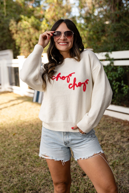 Woman wearing a white sweatshirt with red text and light blue shorts outdoors.