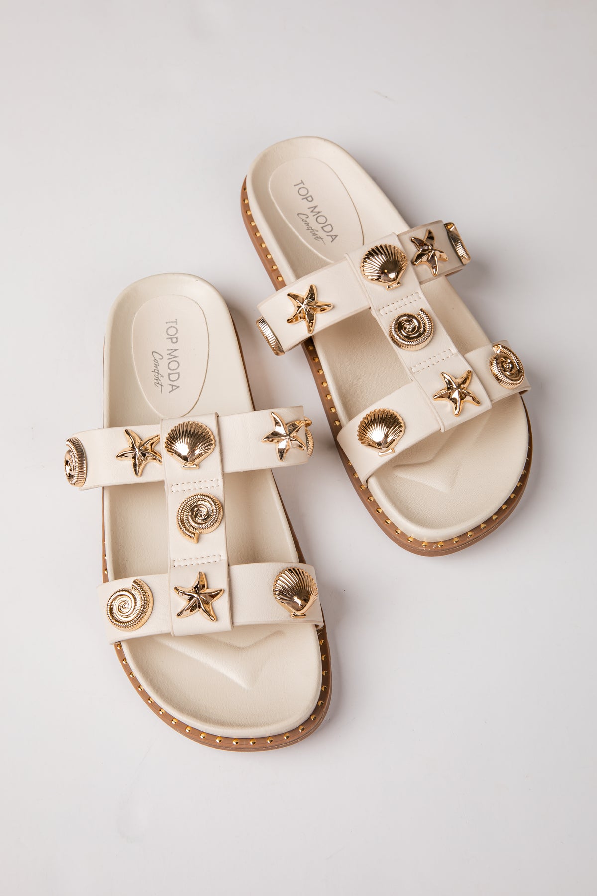 Pair of beige sandals with star and shell decorations on a light gray background