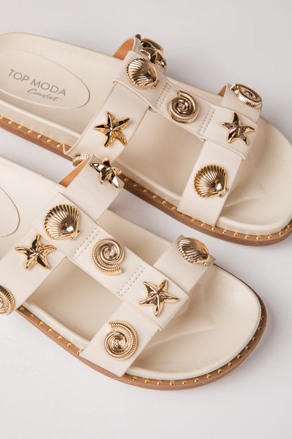Beige sandals with gold embellishments on a light gray background