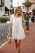 Woman in a white dress walking on a brick sidewalk with buildings in the background