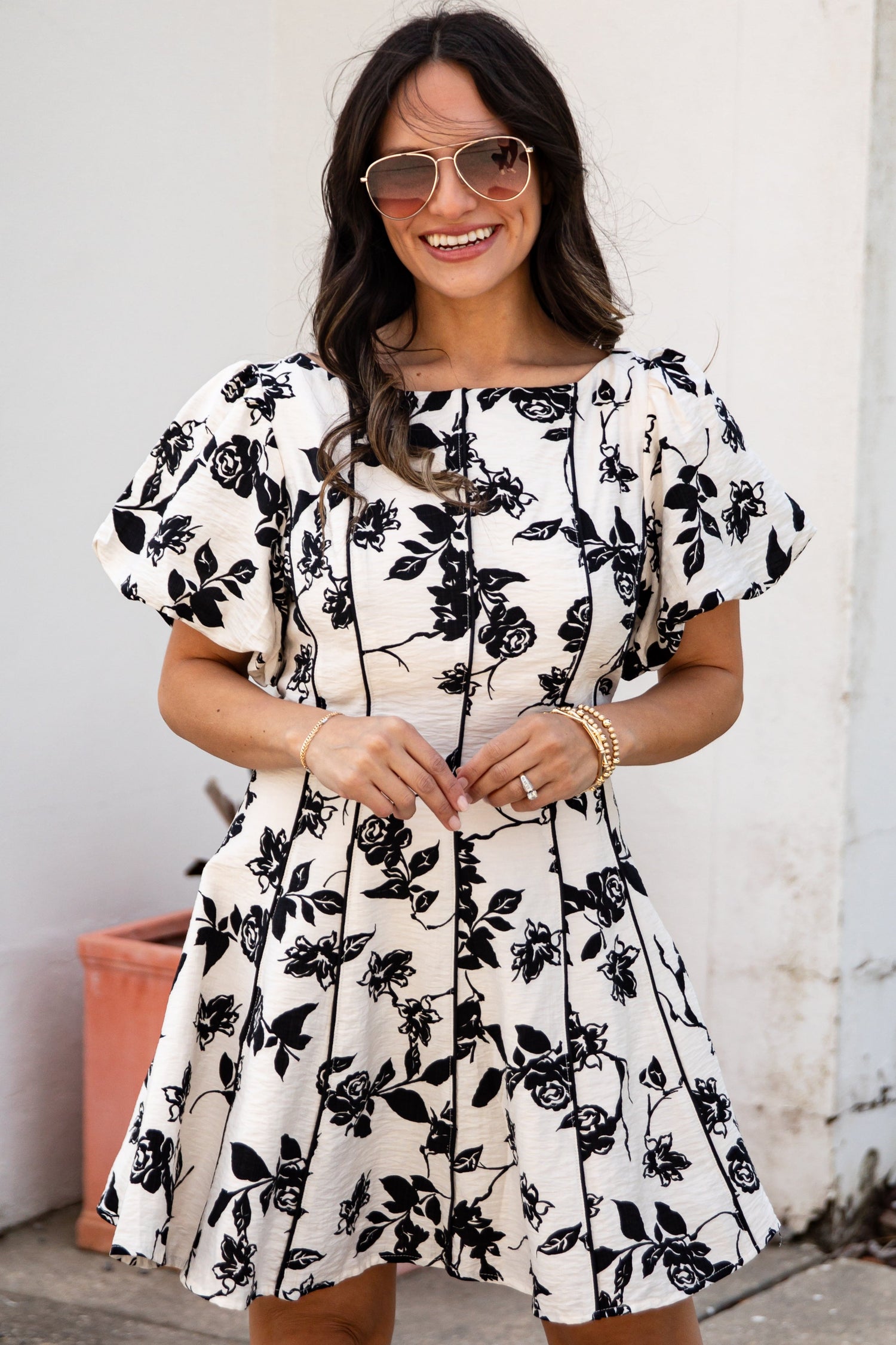 Woman wearing a black floral dress standing against a white wall.