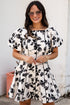 Woman wearing a black floral dress standing against a white wall.