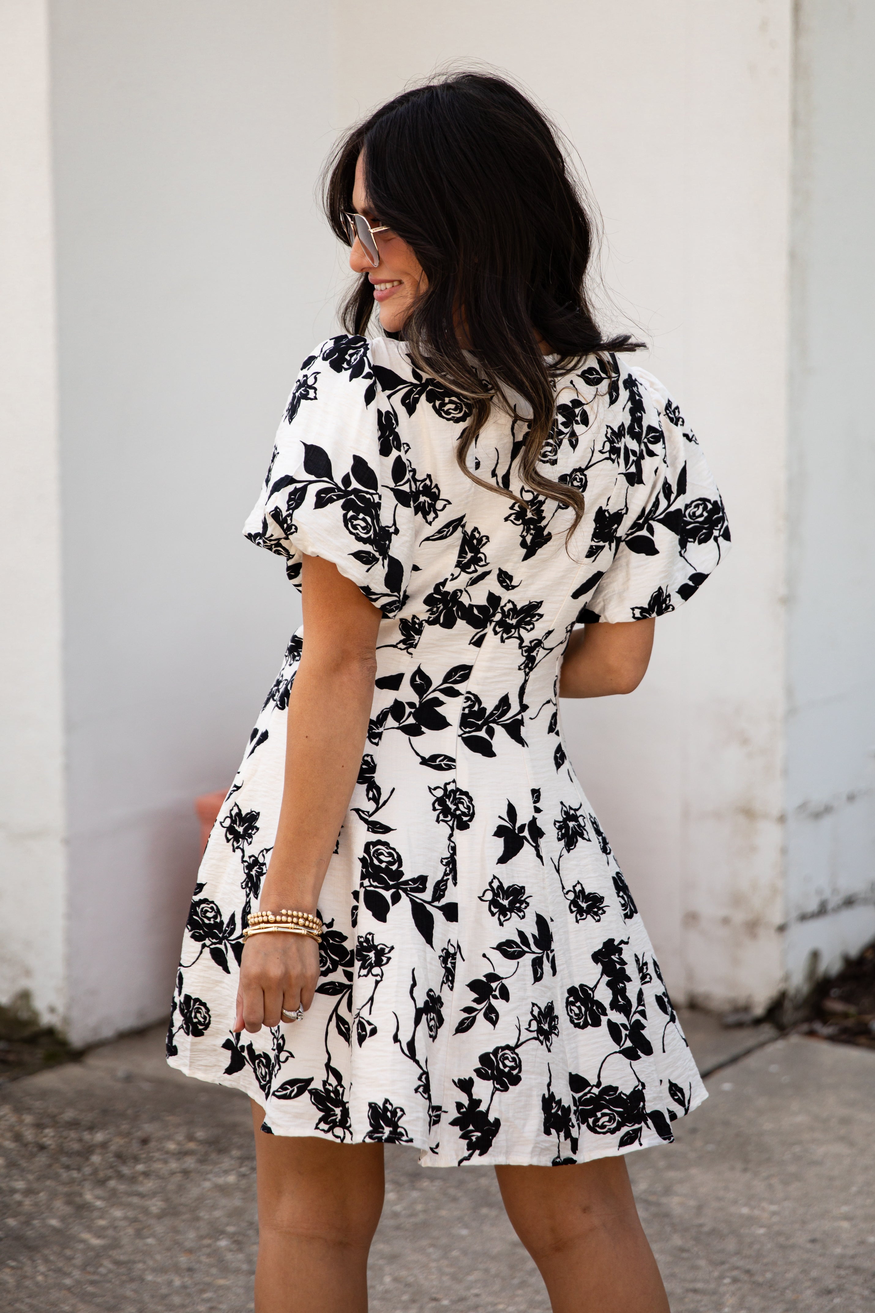 Woman wearing a black and white floral dress against a white wall.
