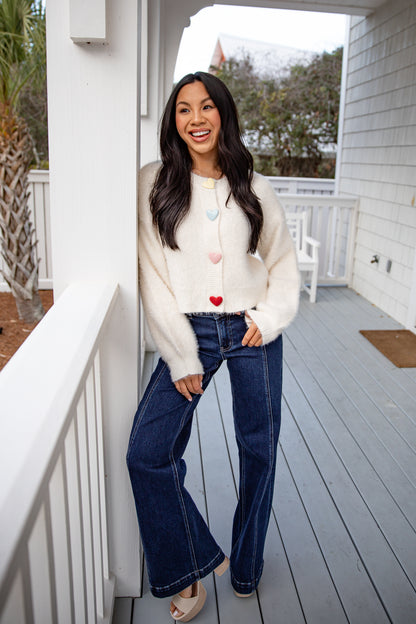 Woman standing on a porch wearing a white cardigan, white top, blue jeans, and sandals.
