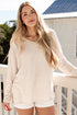 Woman in a beige sweater and white shorts standing on a balcony.