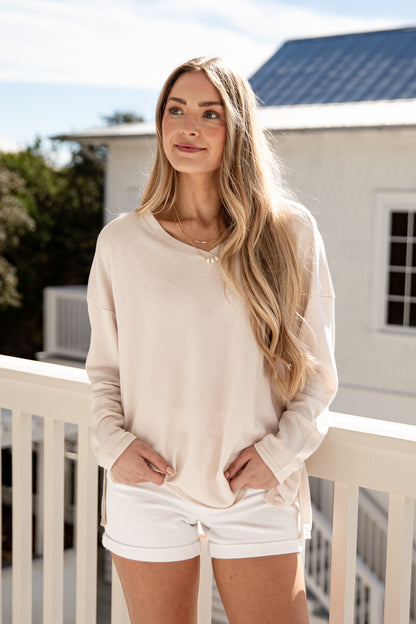 Woman wearing a beige long-sleeve shirt and white shorts on a balcony.