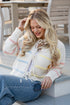 Woman wearing a striped sweater and jeans sitting on a wooden bench.