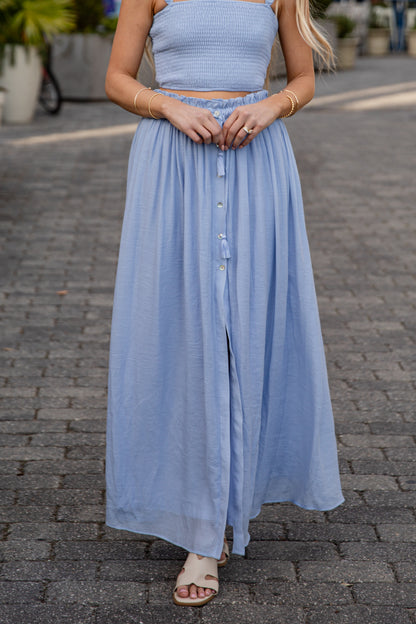 Woman wearing a light blue dress standing on a paved street.