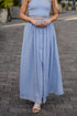 Woman wearing a light blue dress standing on a paved street.