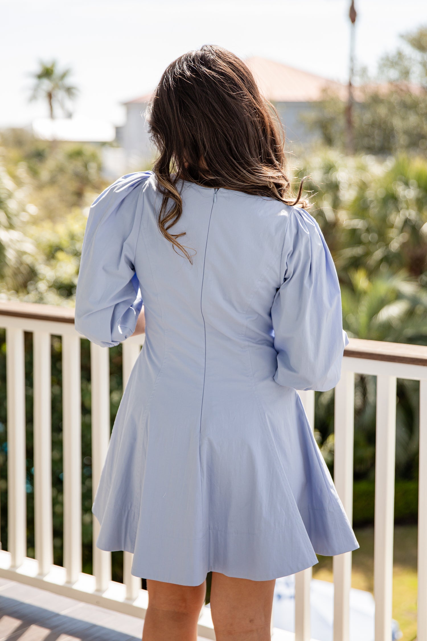Woman wearing a light blue dress on a balcony with greenery in the background
