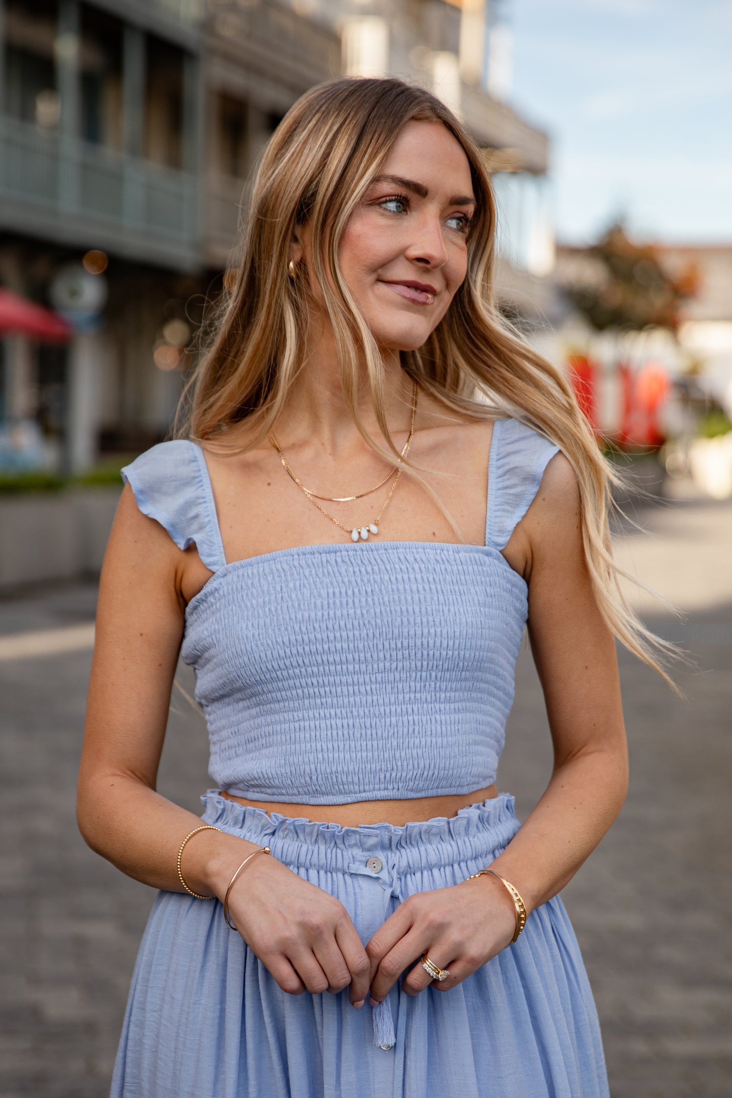 Woman wearing a light blue top and skirt standing on a street.