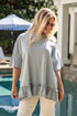 Woman wearing a light gray ruffled top and white pants by a poolside.