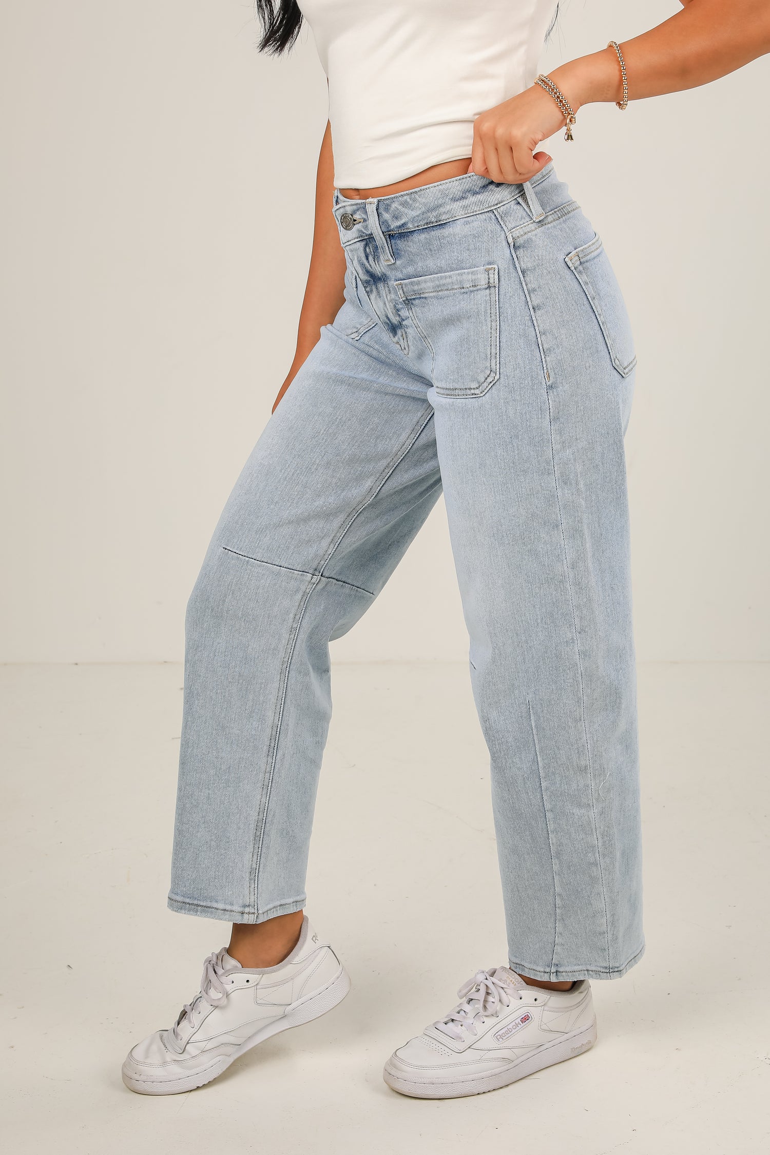 Person wearing light blue jeans and white sneakers on a plain background