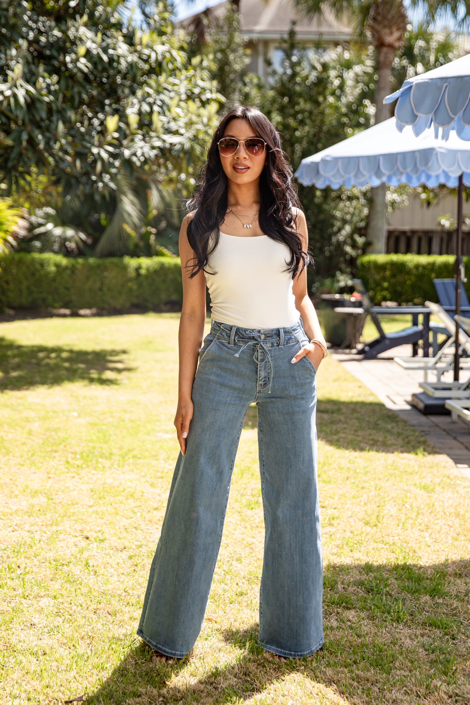 Woman wearing a white top and blue jeans standing in a garden.