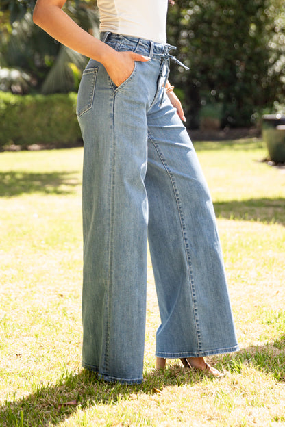 Person wearing light blue jeans standing on grass with trees in the background