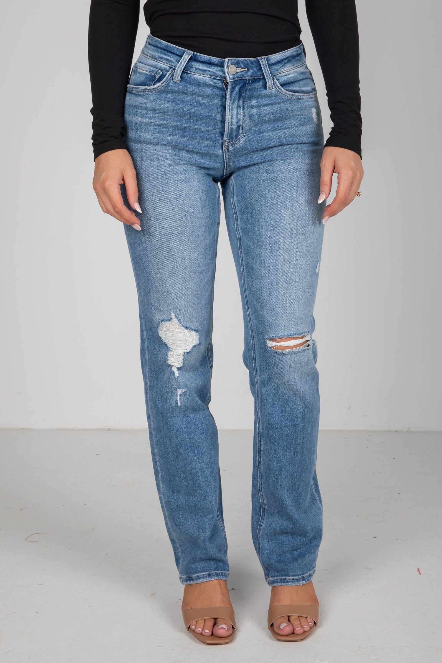 Person wearing blue jeans with distressing details on a plain background