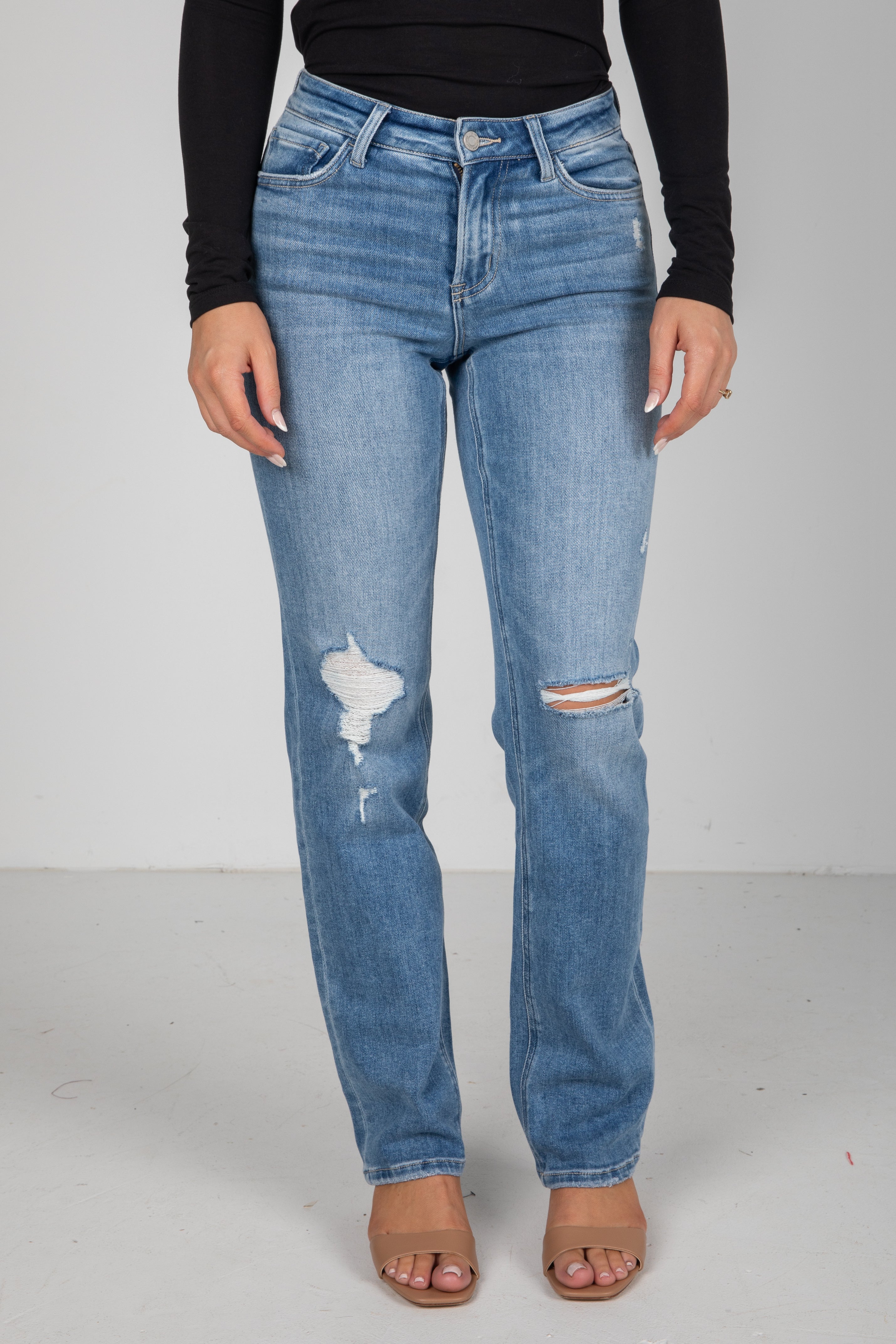 Person wearing blue jeans with distressing details on a plain background