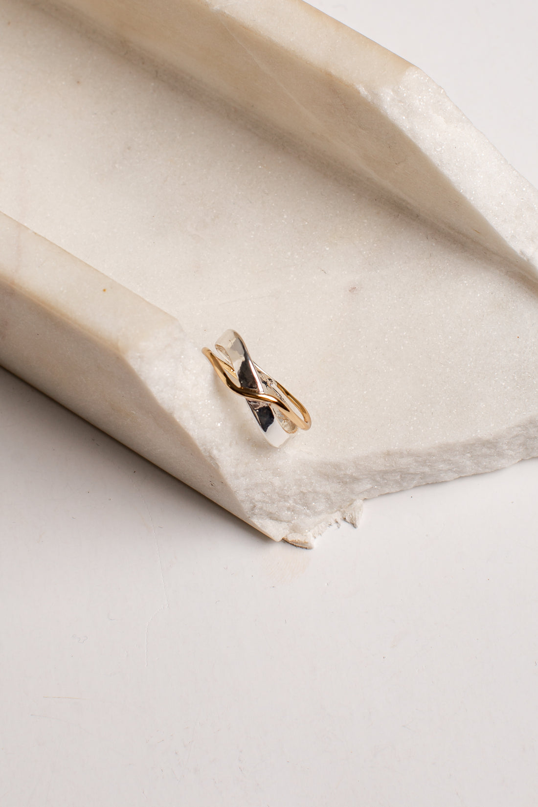 A delicate gold and silver twisted ring resting on a textured, off-white stone surface.