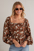 A woman wearing a brown long-sleeve blouse with a white floral print, square neckline, and puff sleeves, paired with blue jeans and round sunglasses, standing against a white brick wall.