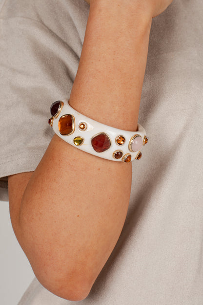 A white ceramic bangle bracelet with various colorful gemstones, worn on a person&