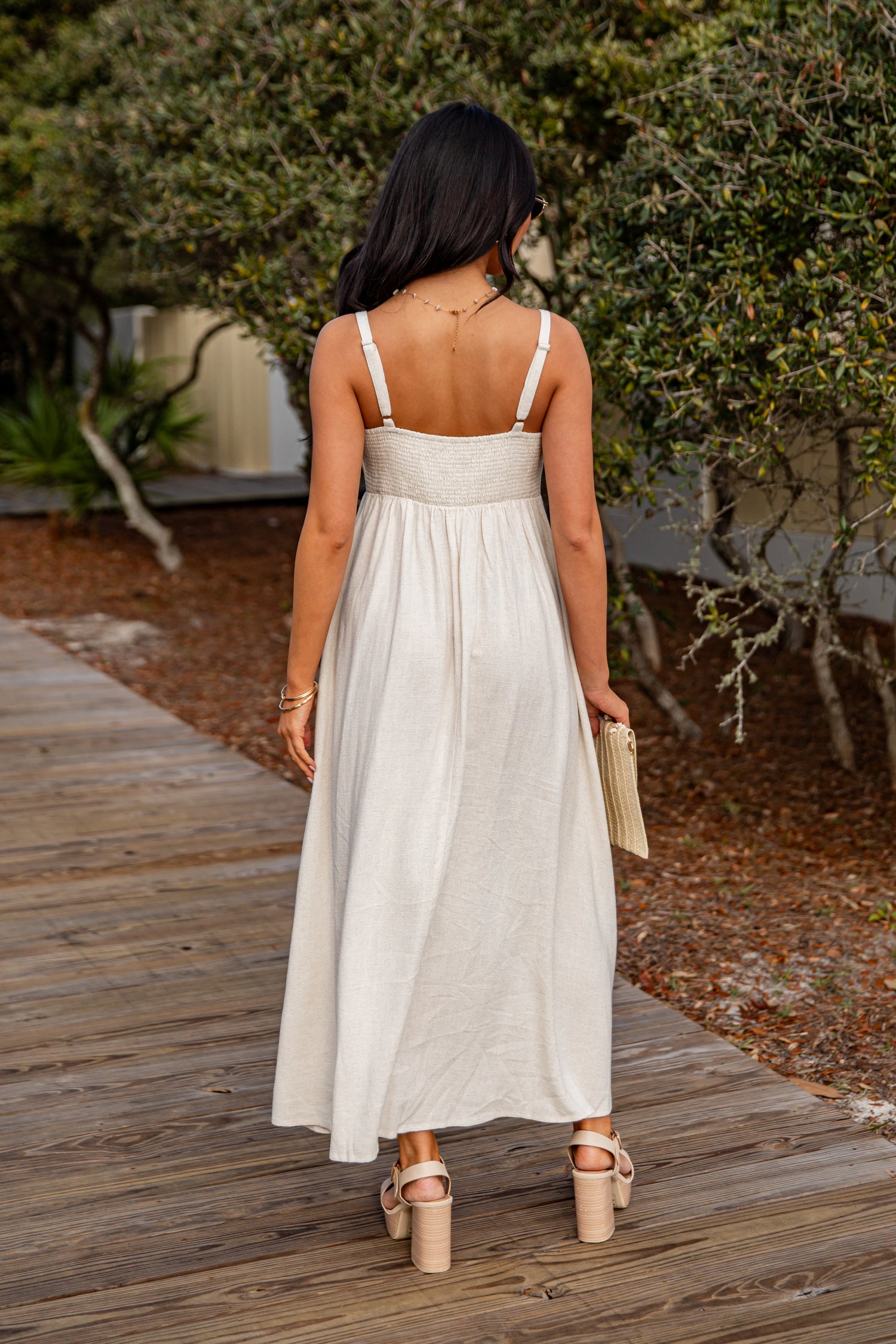 Woman in a white dress walking on a wooden path with greenery in the background