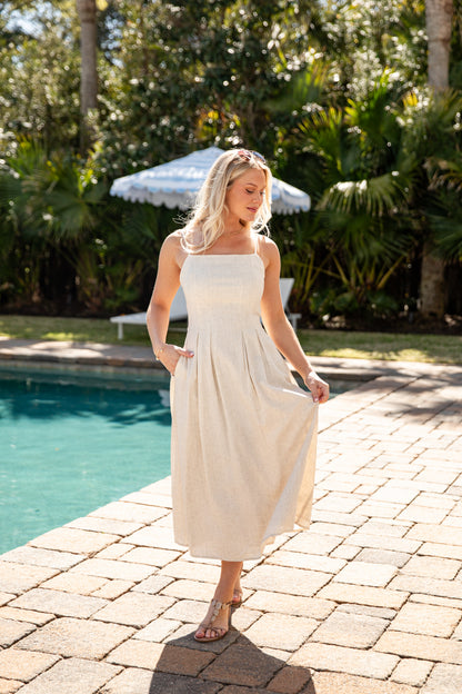 Woman in a white dress standing by a pool with greenery in the background