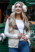 Woman wearing a patterned cardigan, white sweater, and blue jeans standing in front of a green vehicle.