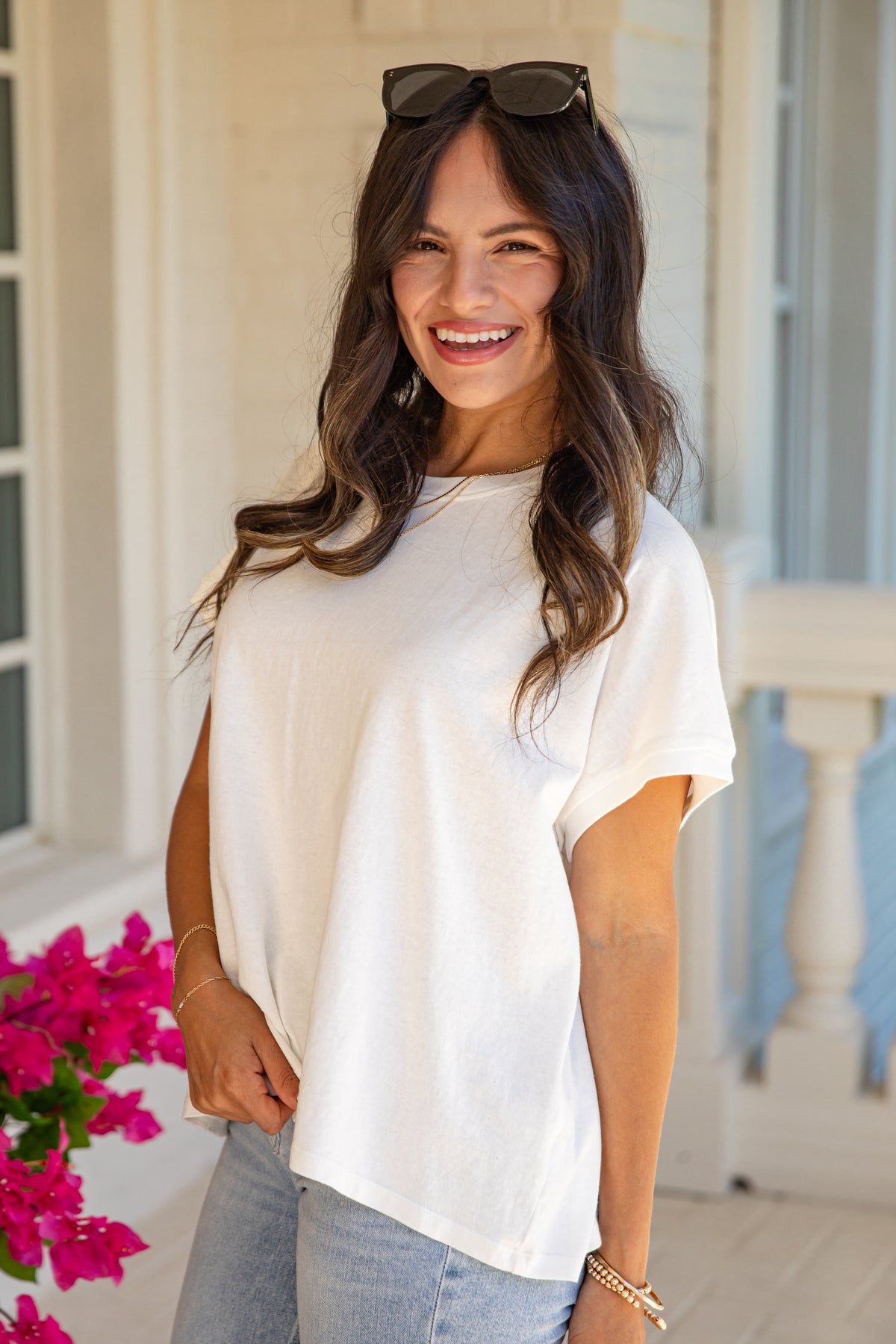 Woman wearing a white t-shirt and sunglasses on her head, standing outdoors.
