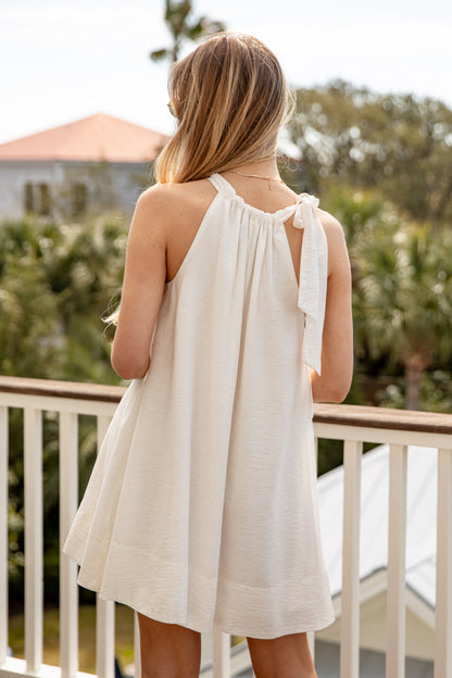 Woman in a white dress standing on a balcony with greenery in the background