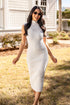 Woman in a white ribbed dress standing outdoors with a house in the background