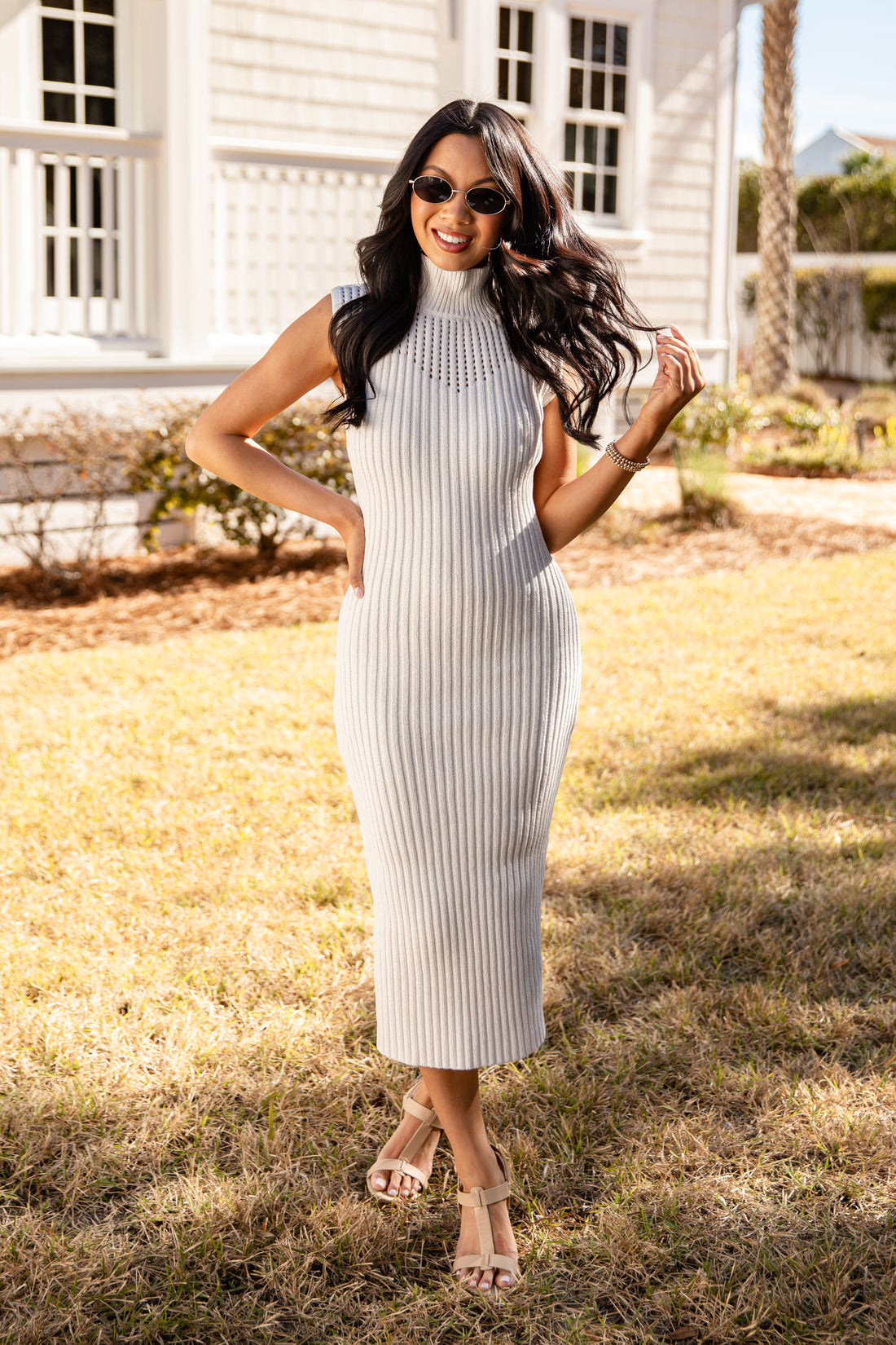 Woman in a white sleeveless dress standing outdoors with a house in the background