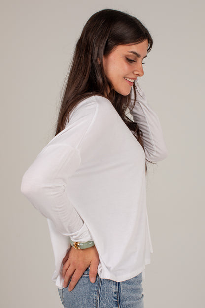 A woman wearing a white long-sleeve knit top and light blue jeans, shown from a side profile against a plain light gray studio background.
