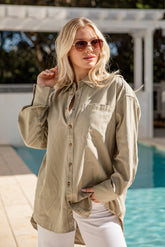 Woman wearing a light green shirt and sunglasses by a pool