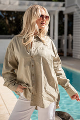 Woman wearing a beige shirt and white pants by a poolside.