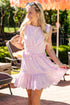 Woman wearing a light pink embroidered mini dress featuring delicate floral eyelet details, a smocked waist, tie shoulder straps, and a tiered ruffle skirt. The feminine silhouette and soft pastel hue make this dress perfect for bridal events, garden parties, brunch dates, and spring-to-summer occasions.