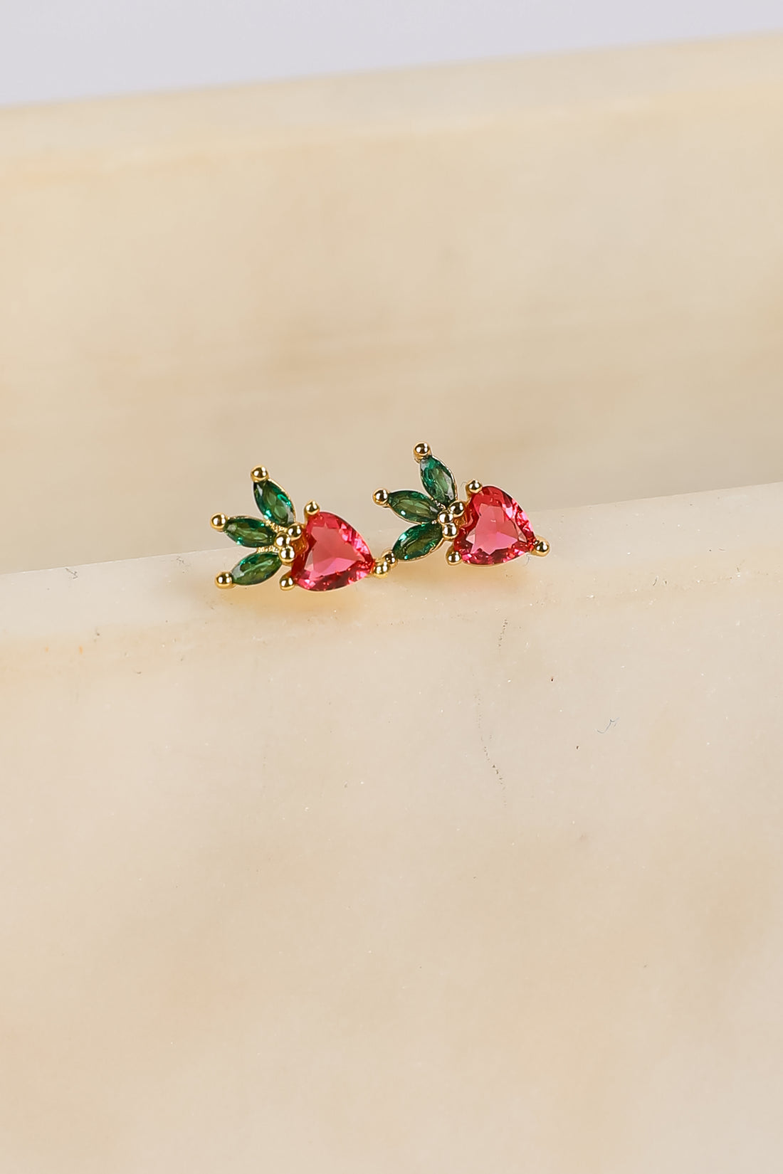 Pair of earrings with heart-shaped gemstones on a beige surface