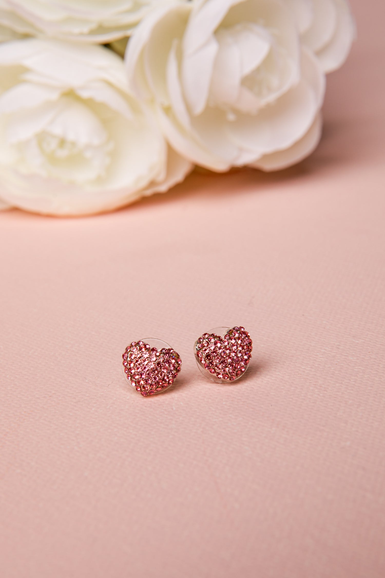 Heart-shaped earrings on a pink surface with white flowers in the background