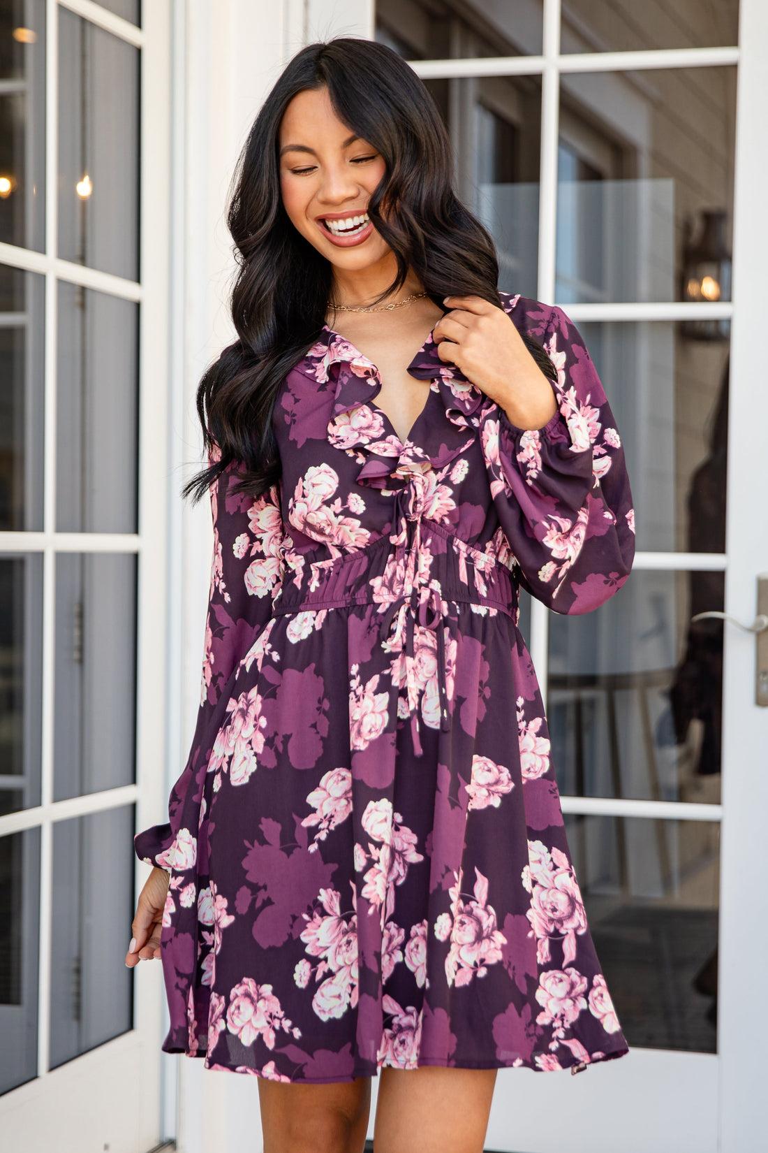 Woman wearing a purple floral dress standing in front of a glass door.