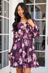 Woman wearing a purple floral dress standing in front of a glass door.