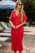 Woman in a red dress standing outdoors with lounge chairs and an umbrella in the background