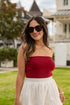 Woman wearing a red top and white skirt with sunglasses outdoors.