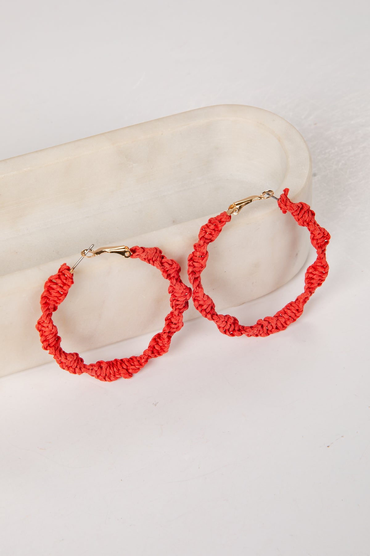 Red hoop earrings on a mannequin arm against a white background