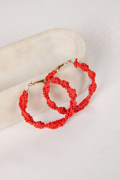 Red hoop earrings on a mannequin arm against a white background