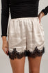 A person wearing satin shorts in a warm off-white/cream color with a black lace hem, paired with a black long-sleeve top. The photo is cropped from the chest down against a light gray background.