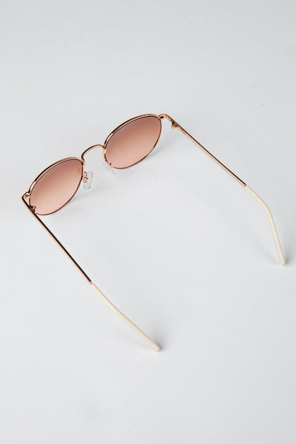 Rose gold sunglasses with pink lenses on a light gray background
