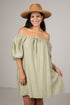 Woman wearing a green off-shoulder dress and brown hat against a plain background