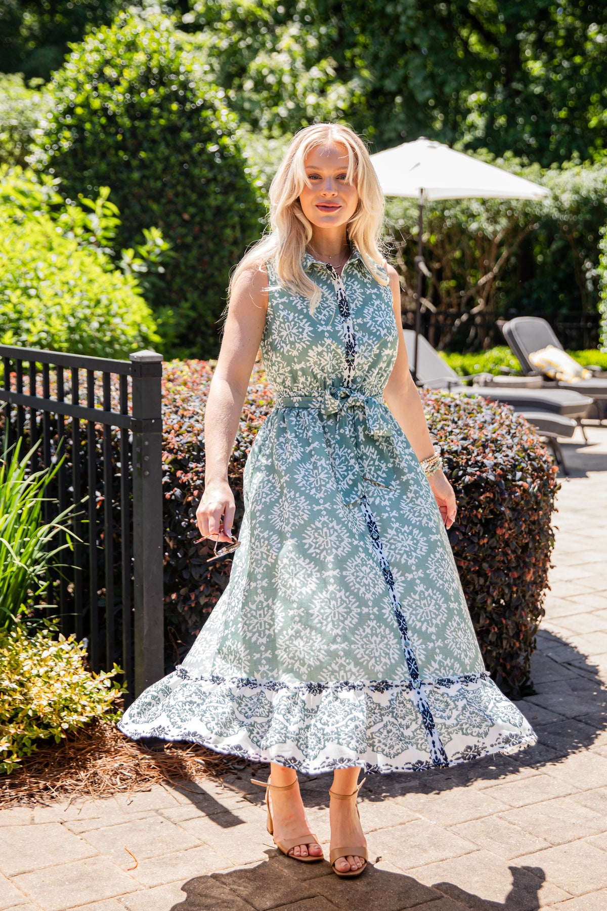 Woman in a floral dress standing outdoors with greenery and a pool area in the background