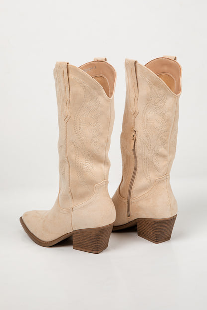 A pair of light beige suede cowboy boots with brown block heels, shown from the back on a clean white studio background.