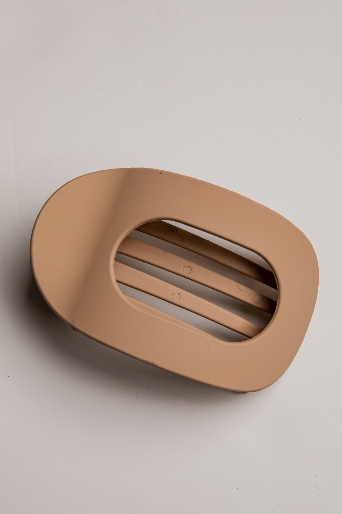 A minimalist, matte beige oval wall-mounted vent or decorative architectural feature with three horizontal slits, shown on a neutral light gray background.